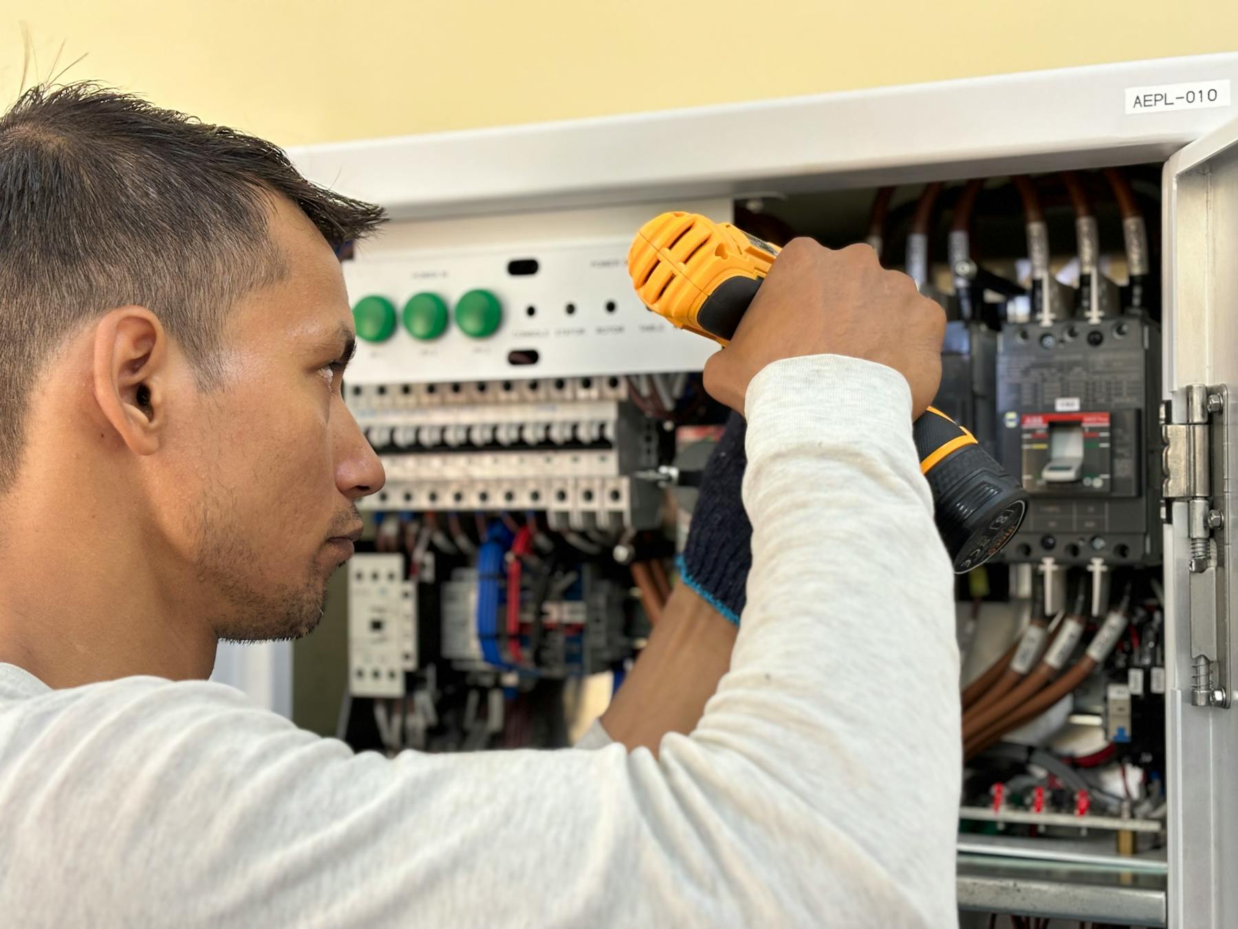 A technician with a drill working on an open electrical switchboard